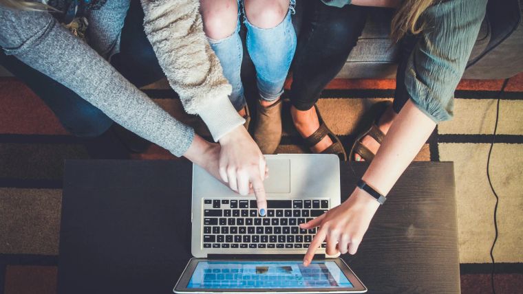Overhead view of several hands working together on one laptop