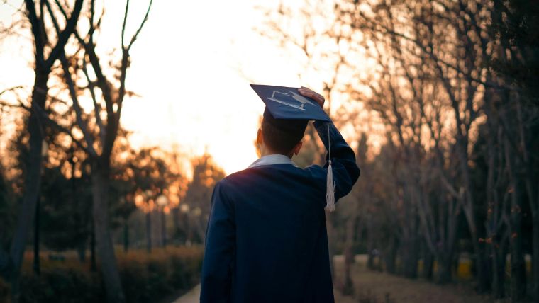 Graduate seen from behind wearing a mortarboard on a path in backlight